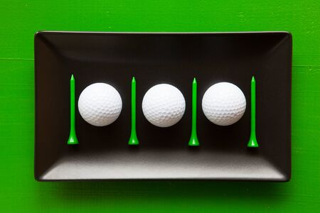 Black ceramic dishes with golf balls and wooden tees on over green background, rectangle dishの写真素材