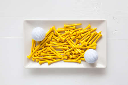 White ceramic dishes with golf balls and wooden tees on over white background, rectangle dishの写真素材