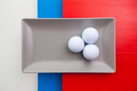 Gray ceramic dish with golf equipments  on over white,blue and red wooden table, rectangle dishの写真素材