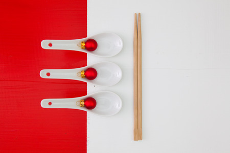 Ceramic spoons and bamboo chopsticks for sushi food and Christmas decoration on the red and white wooden tableの写真素材