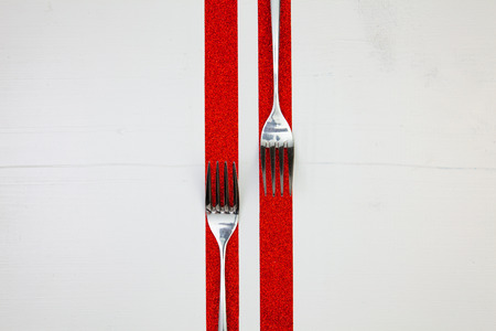 Two forks and red ribbons on the wooden table.