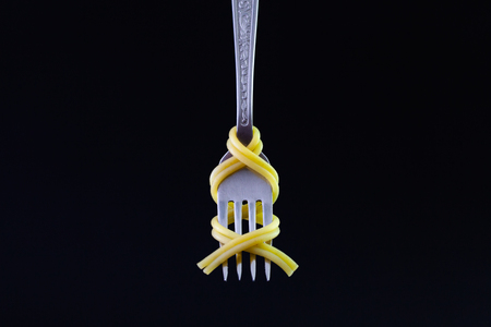 Freshly cooked pasta on a old fork on the black background. Symmetrical loop of spaghetti on an old...