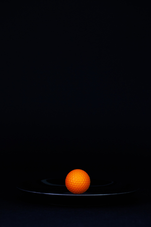 Black plate and  orange golf ball on the black backgroundの写真素材