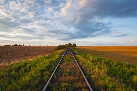 Old Railway tracks running through a field stretch to rural countryside at sunset. Single railway track at sunset, Czech Republicの写真素材