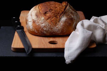 Artisan sourdough bread. Freshly baked round loaf of sourdough bread with linen cloth and knife on black backgroundの写真素材