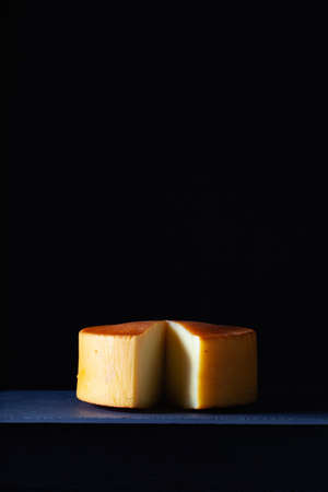 Big round of hard cheese with knife on the slate desk in the dark background.の写真素材
