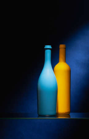 Two empty wine bottles on the glass table in the dark bar.Blue and black empty wine bottles.の写真素材