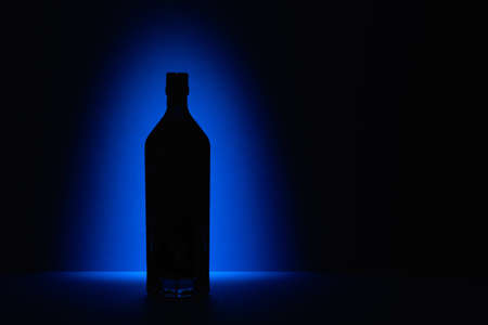 Mysterious bottle on the blue table. Silhouette of a bottle of alcohol on the blue background.の写真素材