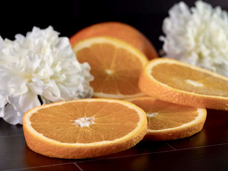 Fresh orange slices and a half orange laying on a black tile counter with two white carnations for decoration.  Fresh citrus fruit Photo with selective focus.の写真素材