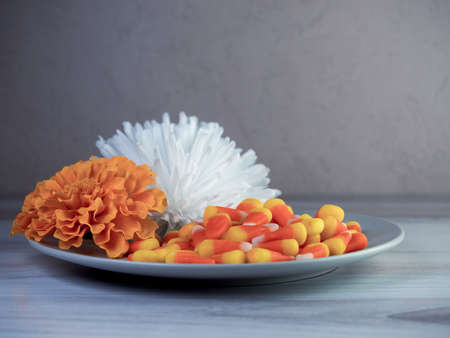 Plate full of orange, yellow and white candy corn for Halloween, garnished with a white and orange...