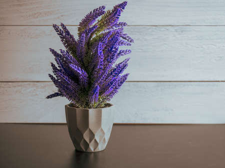 Purple artificial lavender like plant sitting in a black slate surface with a gray shiplap background.  Pretty purple home decor.の写真素材