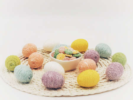 Round placemat topped with Easter eggs covered in sparkly string and a white bowl of pastel colored...