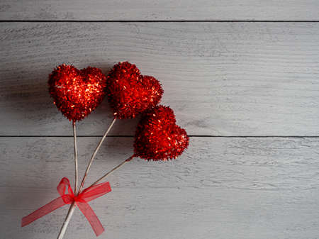 Red sparkly hearts on sticks tied together with a red shear bow against a gray shiplap background,...