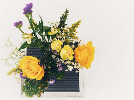 Spring floral arrangement in purple and yellow with roses and other flower blooms sitting on a black...
