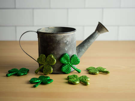 Rustic metal watering can on a natural wood background with white subway tile and green glitter four leaf clovers for St. Patrickâs Day.の写真素材
