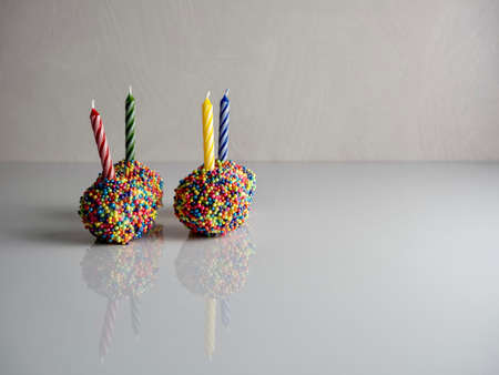 Birthday cake balls, truffle dessert, decorated with white coating and colorful sprinkles, delicious for a celebration on a white surface with a high gloss reflection.の写真素材