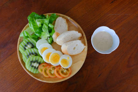 Top view of Sliced egg salad serve with vegetable, kiwi, tomato, crispy bread and separated sesame dressingの写真素材