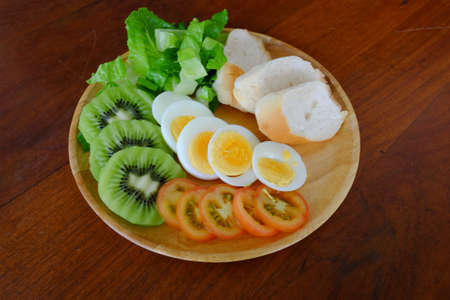 Sliced egg salad serve with vegetable, kiwi, tomato, and crispy bread (on the middle)