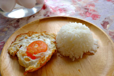 Rice topped with fried salty egg served with stir-fried spicy basil pork and the bolw of salt egg on the tableの写真素材