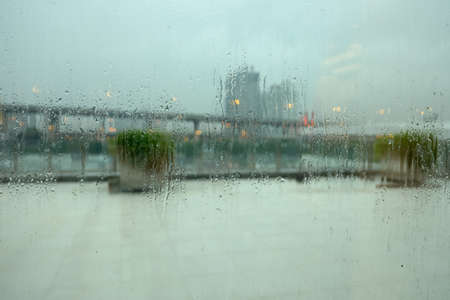 Rain drop on window and bokeh light dot reflection with blurred cityscape view outsideの写真素材
