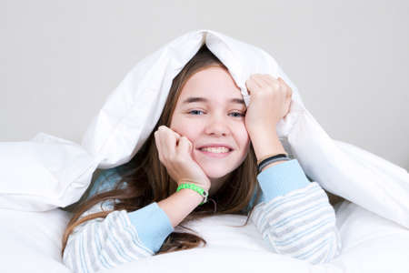Smiling happy girl in bed under the sheets