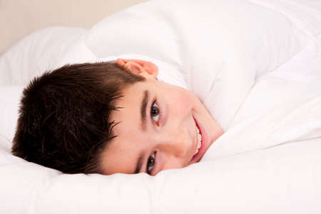 Little boy in bed covered with blanket smiling