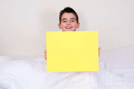 cute little boy with yellow blank board on bedの写真素材