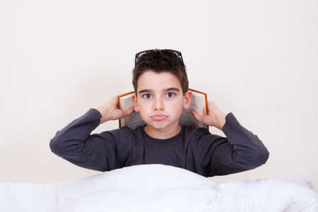 Little boy with book and expressions in bedの写真素材