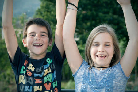 portrait of girl and boy with arms raised in joy.の写真素材