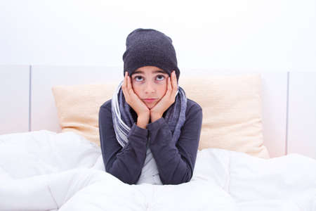 cold child in bed with cap and scarfの写真素材