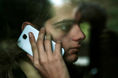 young man talking on mobile phone behind glassの写真素材