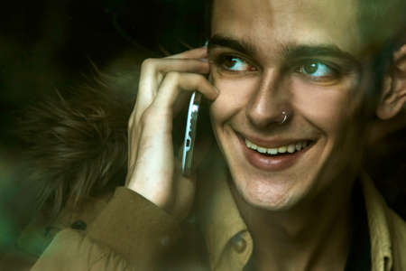 young man talking on mobile phone behind glassの写真素材