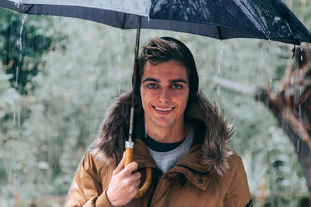 young man with umbrella on rainy dayの写真素材