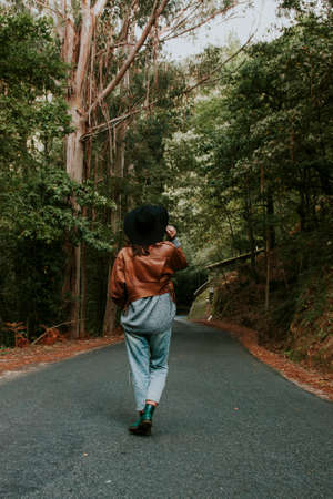 girl with hat walking along the road behind the forest