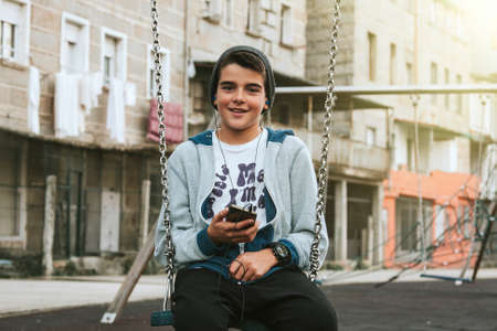 child with mobile phone on swing on city streetの写真素材