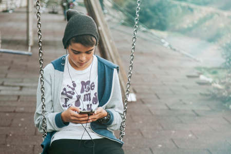 child with mobile phone on swing on city streetの写真素材