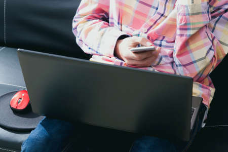 man in house sitting on the sofa with the phone mobile and the laptopの写真素材