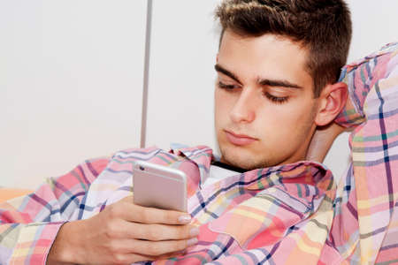 young man with the phone lying in bedの写真素材