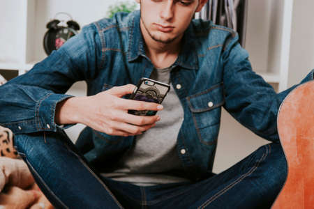 young man with the guitar and the phone in the roomの写真素材