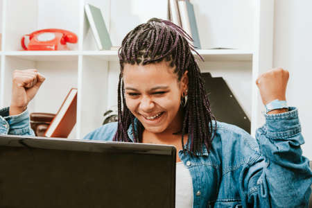female young african descent with the computer in house celebrating with enthusiasmの写真素材