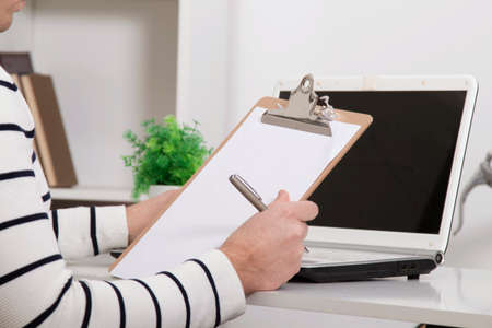 hand with the pen and the folder in the office with the laptop, closeupの写真素材