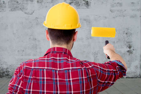 man painting with the brush on bottom of wall