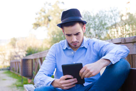 young man modern hipster with the tablet or ebook outdoorsの写真素材