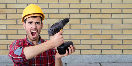 worker with drill screaming rage with the background wallの写真素材