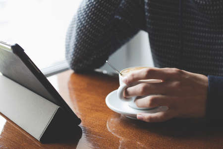 drinking coffee with the tablet, or the digital book on the table in the cafeteria, natural light
