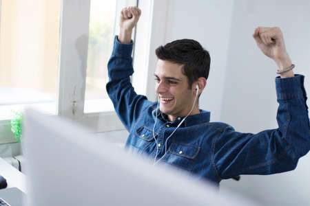 young man celebrating success with headphones and computerの写真素材
