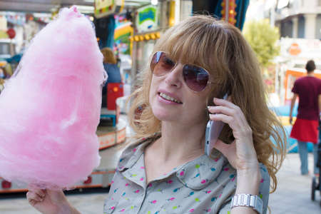 Girl with cotton candy and talking to the phone in amusement park