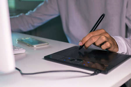 A man's hands working with the digital tablet and computer