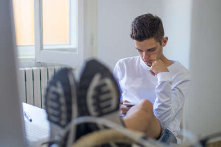 Teenager or young man student on the desktop playing the mobile phone