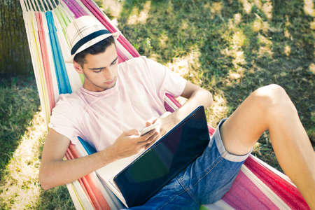 young man or teenager with the laptop in the hammock at sunset summer